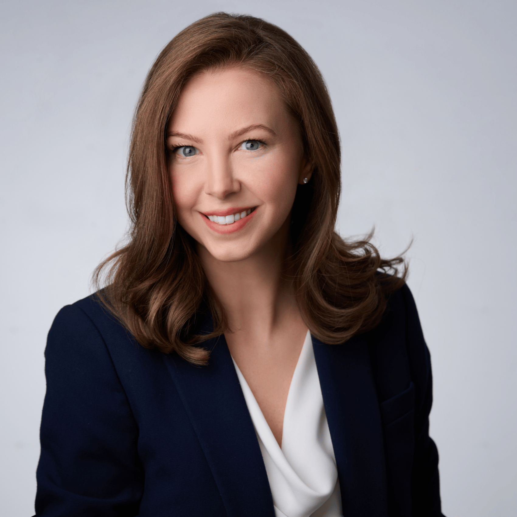 Kathryn Fonda in a dark blue blazer and white blouse smiling at the camera in front of a professional gray background
