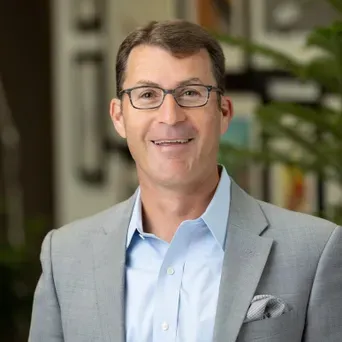 Matt Schwartz smiling at the camera in a baby blue dress shirt and gray blazer