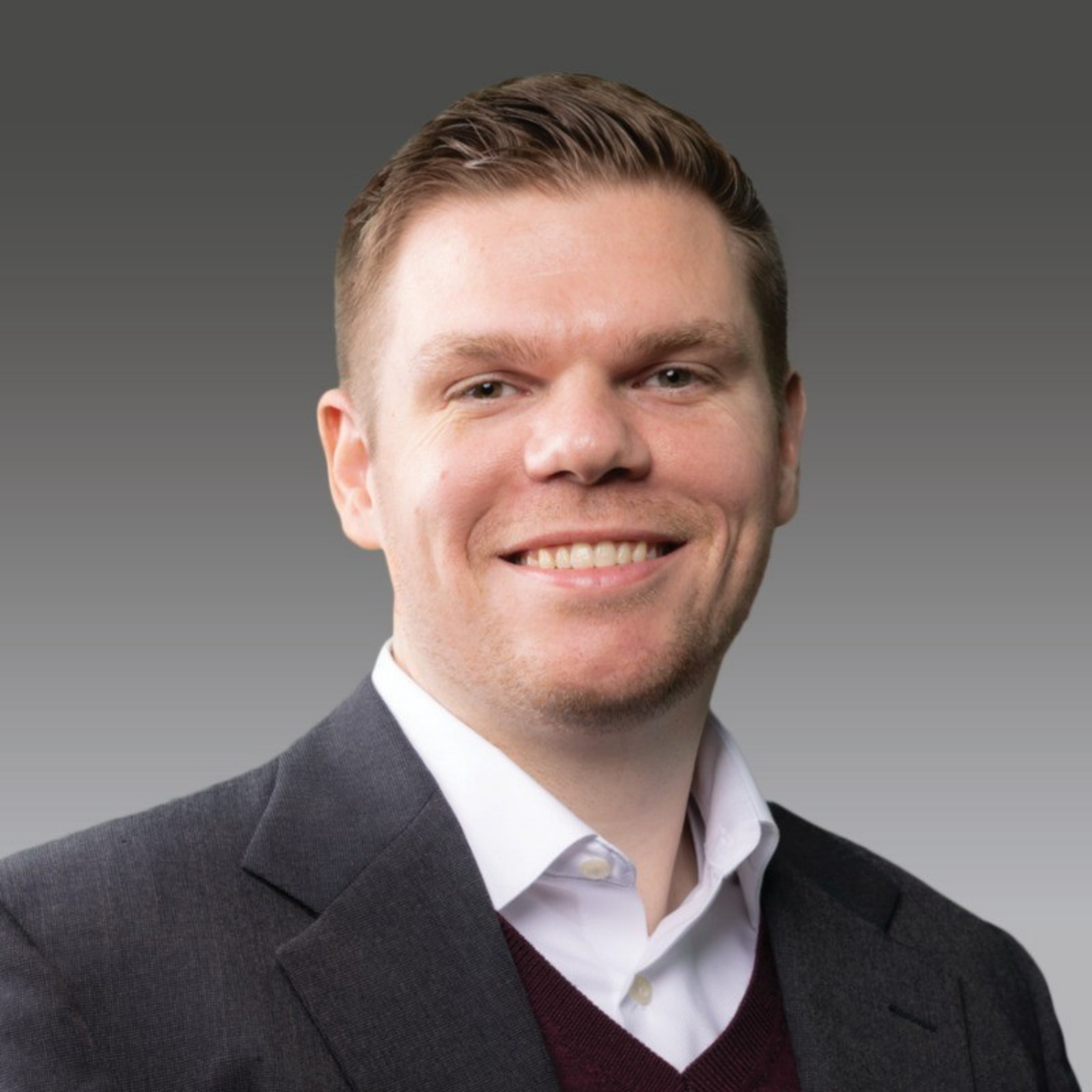 Joe Ritchie smiling at the camera in front of a gradient white to dark gray background