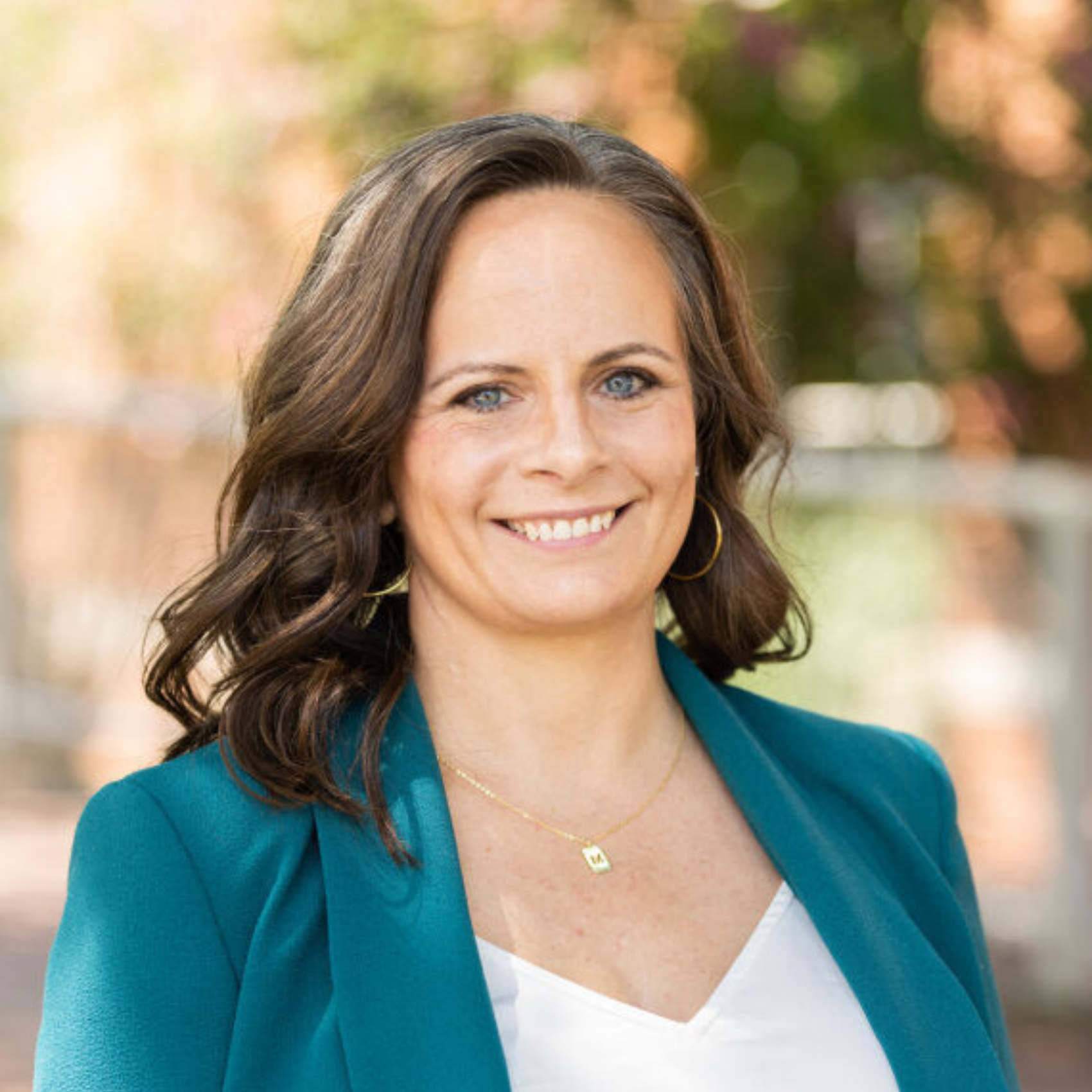 Eliza McCoy in a aquamarine suit jacket and white blouse smiling at the camera in front of a blurred background