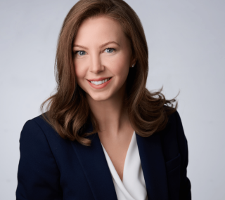Kathryn Fonda in a dark blue blazer and white blouse smiling at the camera in front of a professional gray background