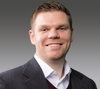 Joe Ritchie smiling at the camera in front of a gradient white to dark gray background