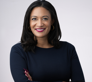 Jennifer in a dark blue long sleeve with her arms crossed while smiling at the camera in front of a gray background